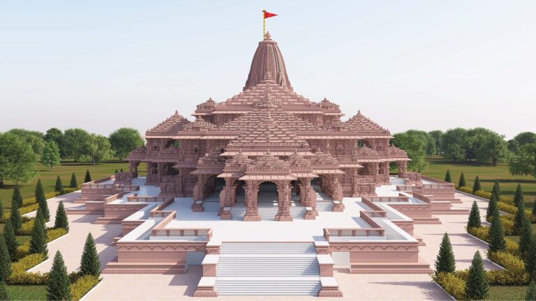 A grand pink sandstone temple with intricate carvings, set amidst landscaped gardens and a clear sky background.